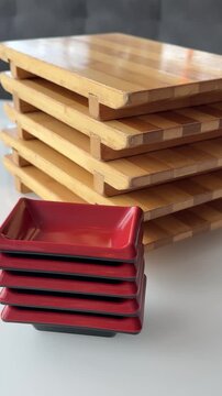 Stacked wooden boards with red rectangular soy sauce dishes arranged on a white table ready for serving asian food and sushi