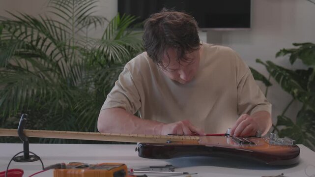 Hands assembling and wiring pickup on sunburst electric guitar through mid to late sequence