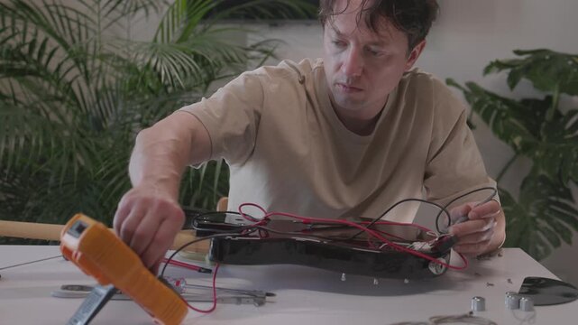 Male luthier performing stepwise electric guitar repair and testing in home workshop through