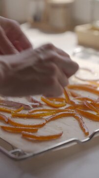 Hand removes candied orange peel from parchment paper on a tray after drying. Concept of homemade citrus candy and sweet food process
