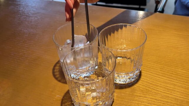 Serving ice cubes with metal tongs into drinking glass on wooden table