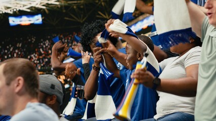 Obraz premium Black family celebrating with young child during exciting soccer match in packed stadium, cheering for blue team, parents sharing excitement of live sports with child fan, childhood joy.