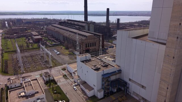 Aerial drone view of a large coal-fired power plant with towering smokestacks, turbine halls, conveyor systems, and industrial infrastructure. Wide overhead perspective of an electricity generation fa