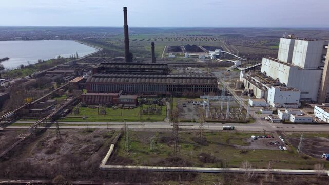 Aerial drone view of a large coal-fired power plant with towering smokestacks, turbine halls, conveyor systems, and industrial infrastructure. Wide overhead perspective of electricity generation.