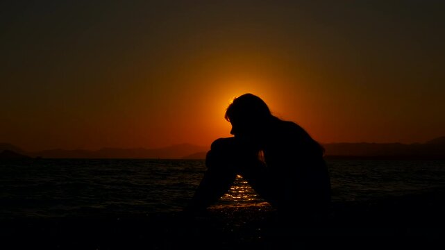 Girl sitting on shore against orange horizon. An alone girl sitting on empty bay and waiting for somebody during sunset time