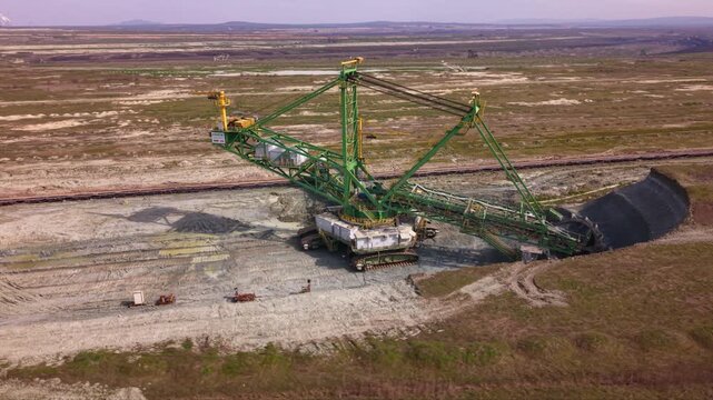 Aerial drone view of a giant bucket-wheel excavator extracting overburden in a large open-pit surface mine. Massive mining machinery cuts through layered earth.