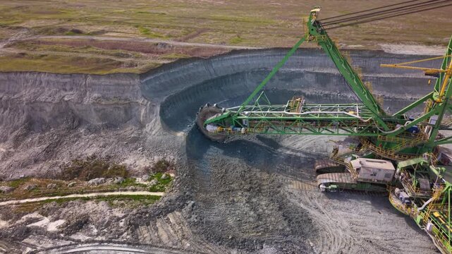 Aerial drone view of a giant bucket-wheel excavator extracting overburden in a large open-pit surface mine. Massive mining machinery cuts through layered earth.