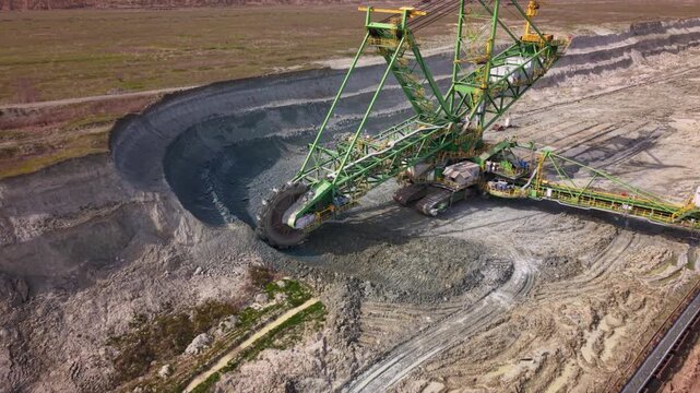 Aerial drone view of a giant bucket-wheel excavator extracting overburden in a large open-pit surface mine. Massive mining machinery cuts through layered earth.
