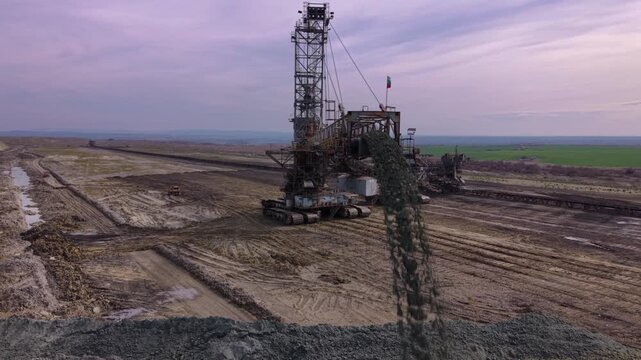 A large bucket-wheel excavator working in an open-pit mine, with conveyor structures, terraced earth, and a wide industrial landscape