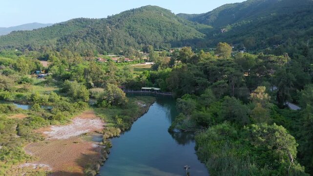 Azmak River winding through lush green vegetation, wetlands, and forested hills near &Ccedil;amlı Village in the Marmaris region, Turkey. Aerial drone shot 