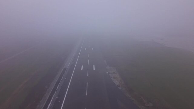 Aerial view of an airport runway almost completely obscured by dense fog, with only faint runway threshold markings and pavement visible through extremely low-visibility weather conditions.