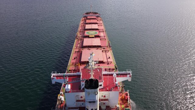 Aerial view from above a cargo ship&rsquo;s deck with large hatch covers and a helipad marking, sailing on open water