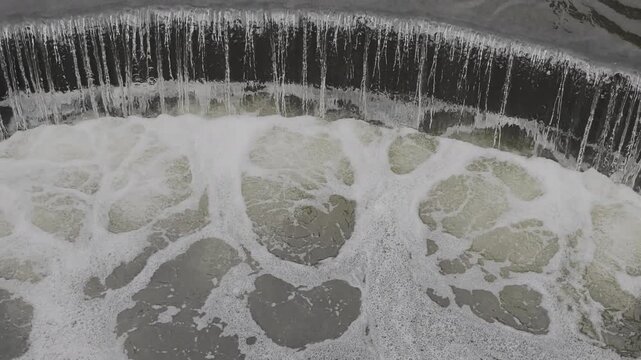 Close up view of water cascading over a curved weir, creating turbulent foam. The powerful current symbolizes clean, renewable energy