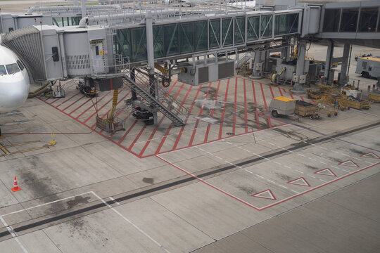 Airport jet bridge connected to airplane on concrete tarmac at terminal gate area with equipment