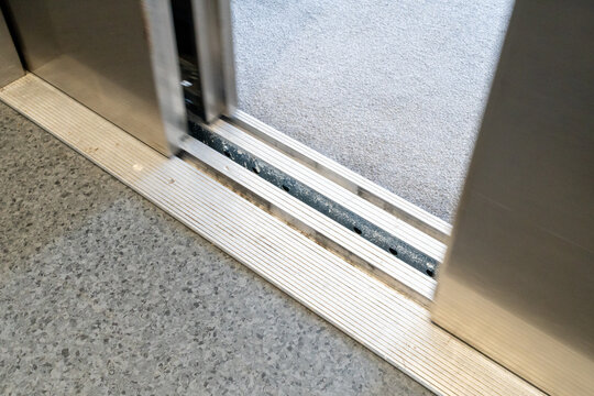 Open elevator door with metallic threshold and gray textured floor indoors