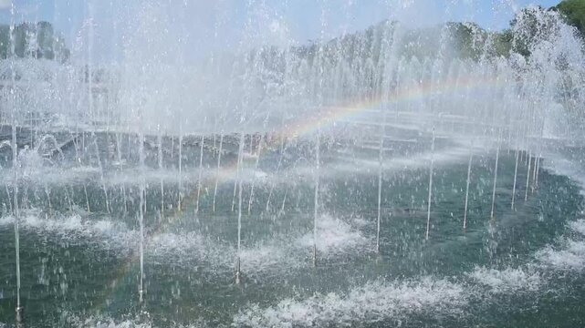Rainbow over city fountain water splashes in summer park