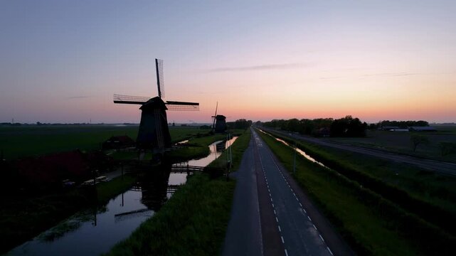 Dutch windmills silhouette along a canal at sunset