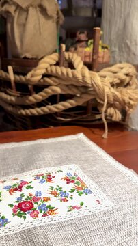 Close-up embroidered tablecloth on wooden table, colorful floral band, visible stitch texture, coiled rope decor, cozy rustic