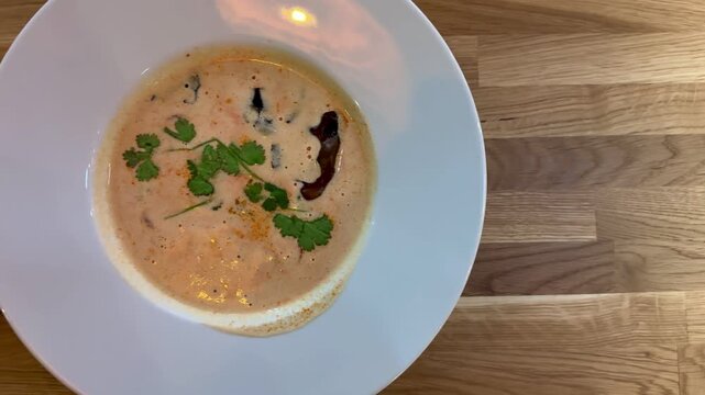 Creamy mushroom puree soup white plate on wooden table restaurant closeup, garnished with herbs and mushroom slice, warm natural