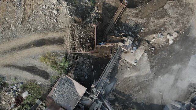 Aerial view of industrial conveyor belts and stone crushing machinery processing gravel and rocks at a quarry site in Patikraja, Central Java, Indonesia.