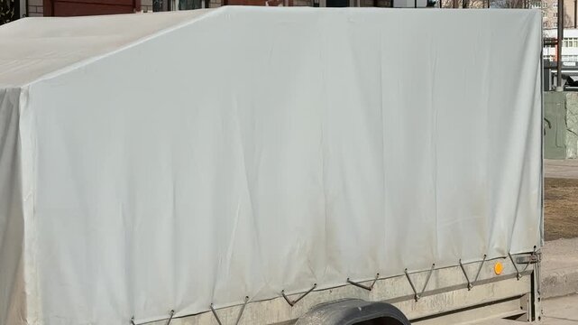 Tarp covered trailer parked on asphalt dirty after long trip, closeup of mud splattered wheel and bent fender, canvas secured