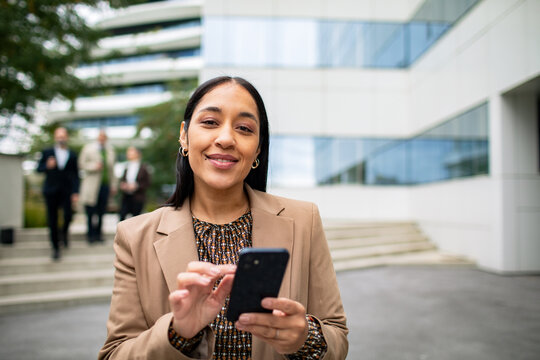 Smiling businesswoman using smartphone outside modern office