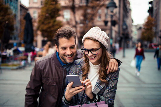 Happy couple using smartphone while shopping in city