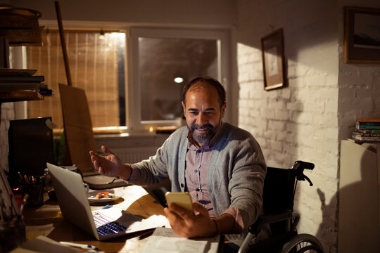 Man in wheelchair working from home on smartphone video call at night