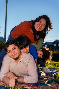 Playful Hispanic family piled on blanket outdoors.
