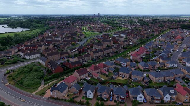 Aerial view of a modern residential neighborhood with brick houses and rooftops under a cloudy sky with Ely Cathedral in the distance in Ely, England, United Kingdom.
