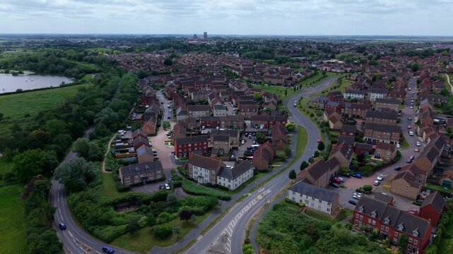 Aerial view of modern residential houses and winding roads surrounded by lush green trees and a distant cathedral, Ely, England, United Kingdom.
