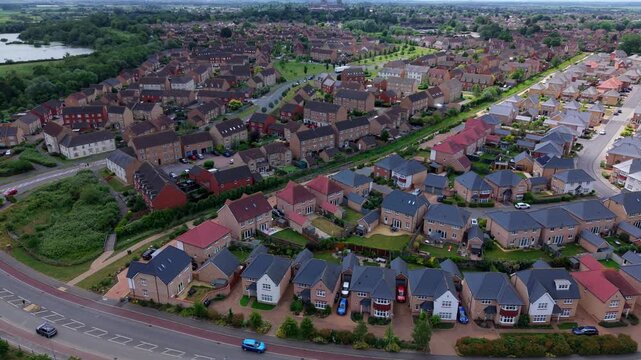 Aerial view of a modern residential housing estate with brick houses and gardens near a lake in Ely, England, United Kingdom.