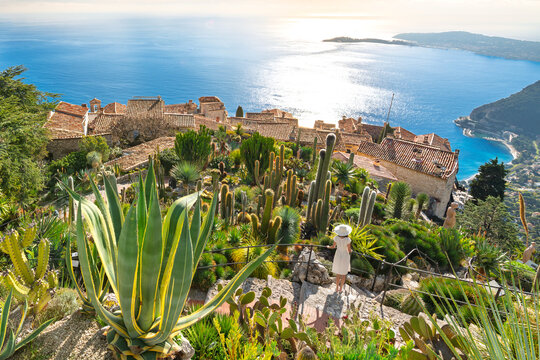 A female tourist stands on a narrow stone staircase of the botanical garden looking down on the medieval hilltop village of Eze Village, on the Mediterranean Coast of Southern France.