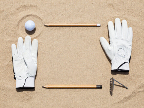 Golf Accessories Stock Layout Golf ball, glove, scorecard pencil and bunker rake arranged neatly on sand, top-down view, clean commercial stock composition, 