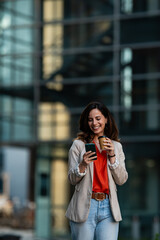 Fototapeta premium Professional woman smiling using smartphone drinking coffee in city