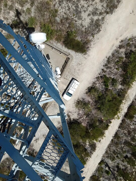 HD Aerial view from industrial communication tower over service vehicle, sandy access road, and coastal vegetation in Western Cape, South Africa.
