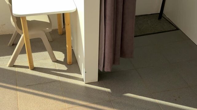 Mid sequence retail scene captured from top view showing children's play table and small chair positioned left-center foreground partially inside dressing room alcove next to hanging