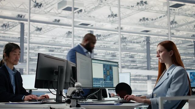 Man and woman review microchip production operations inside factory workplace with PC software, experts in R&D office working to improve semiconductor hardware performance for semiconductor research.