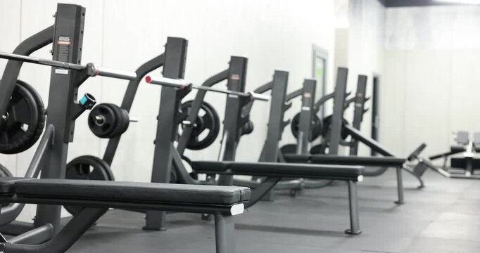 Row of bench press stations with plates in gym. Camera moving right