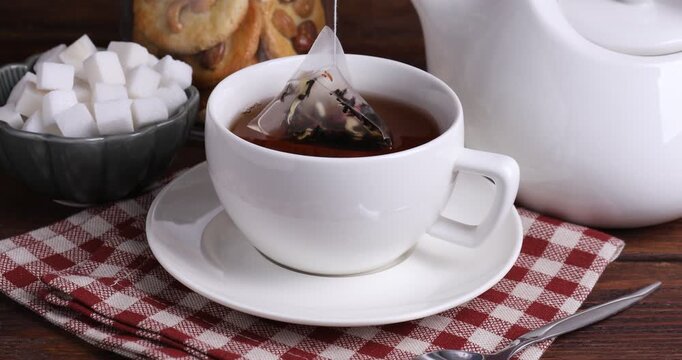 Making tea. Woman putting teabag into cup with hot water and adding sugar at wooden table, closeup
