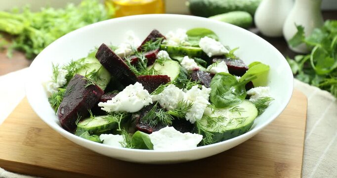Tasty salad with boiled beets, cucumbers, feta cheese and dill spinning on wooden table, closeup