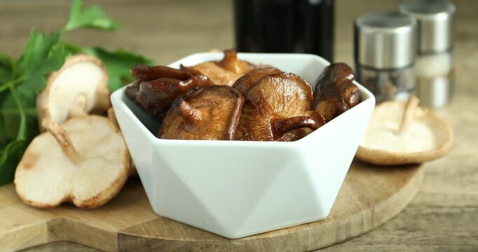 Taking tasty shiitake mushroom from bowl on wooden table, closeup