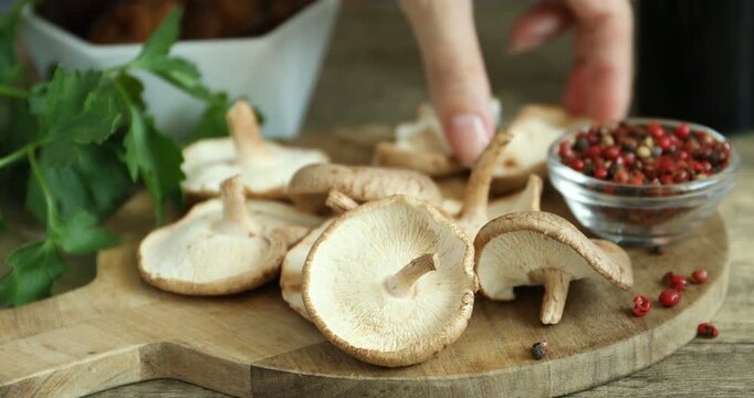 Woman cutting raw shiitake mushrooms at wooden tiled table, closeup