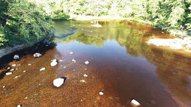 Drone Slowly Moving Down a Shallow River With Brown Water, Exposed Rocks and Forest Reflections on a Sunny Spring Afternoon on the Contoocook River in Henniker, NH