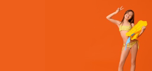 Happy young girl in polka dot bikini holding yellow flippers making peace sign on orange background, she is smiling with closed eyes, enjoying a summer vacation © Pixel-Shot