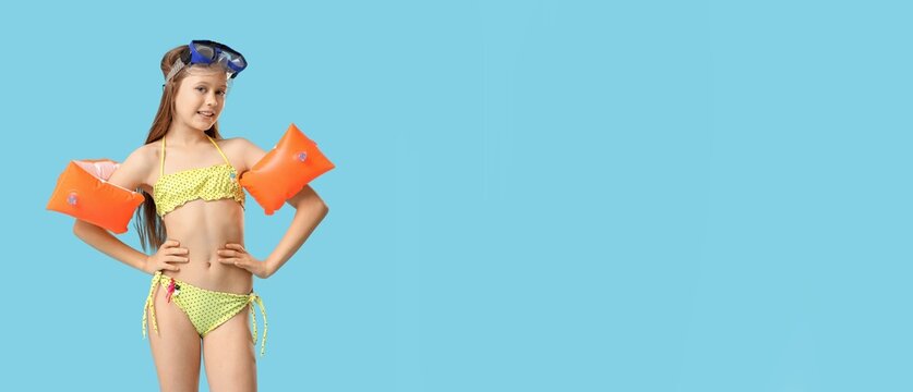Young girl in yellow polka dot bikini with orange armbands and swim goggles ready for summer swimming fun, she smiles at the camera, embodying the joy and excitement of childhood vacations