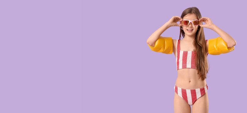 Happy young girl in striped swimsuit and armbands with pink goggles ready for summer swimming fun, she smiles brightly, ready for summer swimming activities