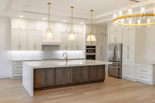 Perspective view of luxury modern kitchen featuring a large central island with waterfall countertop, gold pendant lights, and high-end cabinetry