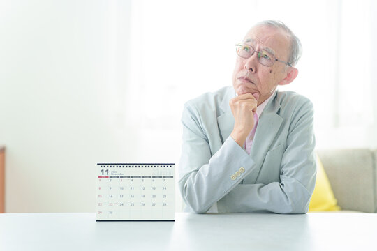 カレンダーの前で困った表情の高齢者の男性