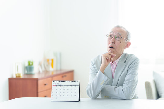 カレンダーの前で困った表情の高齢者の男性